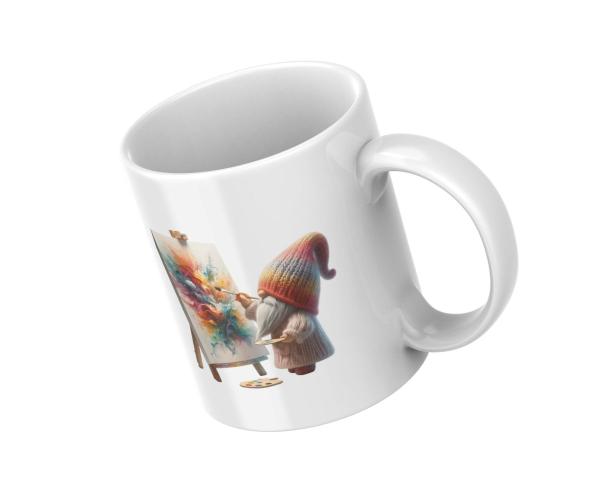 Weißer Keramikbecher mit einem Motiv eines kleinen Gnoms, der mit Pinsel und Palette vor einer Staffelei ein lebhaftes, farbenfrohes Kunstwerk malt. Perfektes Geschenk für Kunstliebhaber und kreative Seelen.