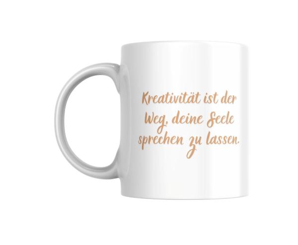 Weißer Keramikbecher mit der Aufschrift ‚Kreativität ist der Weg, deine Seele sprechen zu lassen‘ in sanfter, geschwungener Schrift. Ein inspirierendes Geschenk für kreative Köpfe.