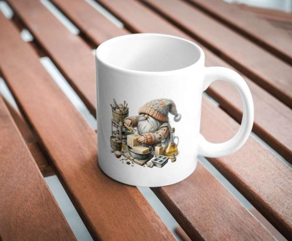 Weißer Keramikbecher mit einem Motiv eines Gnoms in Strickkleidung, der handgemachte Seifen herstellt. Der Becher steht auf einem Holztisch und ist perfekt für Liebhaber von Handwerkskunst und Kreativität.