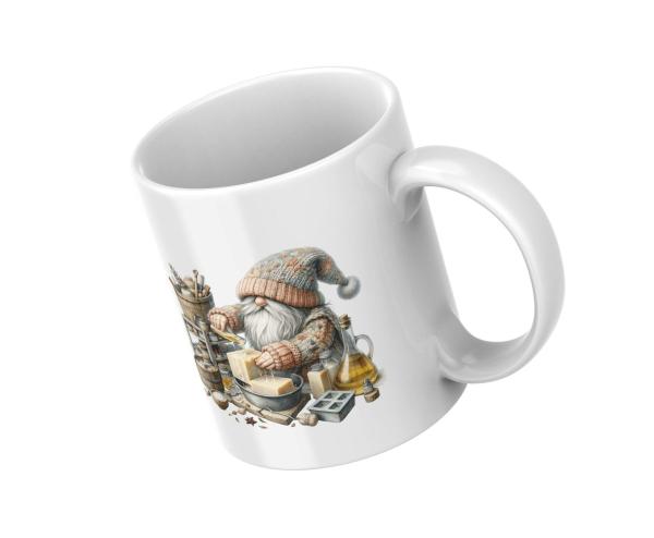 Weißer Keramikbecher mit einem Motiv eines Gnoms in gestricktem Pullover und Mütze, der in einer Werkstatt handgemachte Seife herstellt. Der Becher eignet sich ideal als Geschenk für Liebhaber von Handwerkskunst und Kreativität.