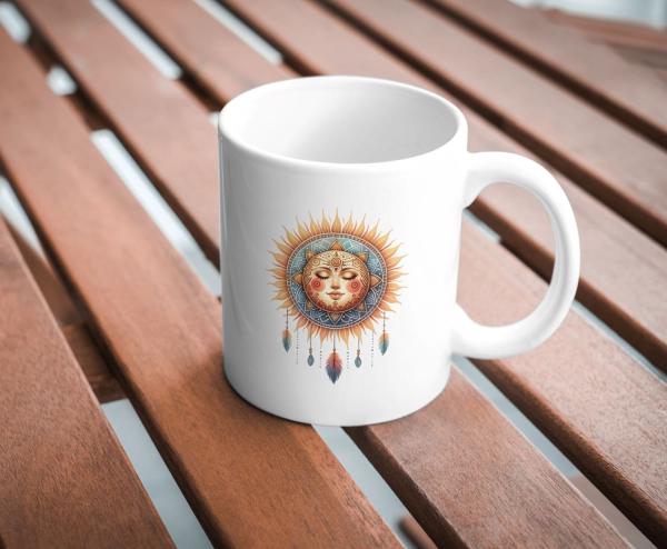 Weißer Keramikbecher mit einem Boho-Sonnenmotiv, das ein lächelndes Gesicht umgeben von strahlenden Sonnenstrahlen, Federn und dekorativen Details zeigt. Der Becher steht auf einem Holztisch und ist ideal für Liebhaber spiritueller Symbole und boho-inspir