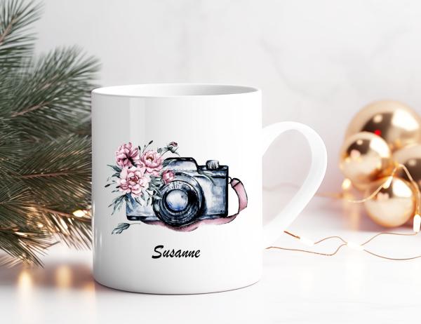 Personalisierte Fotografin-Tasse mit Aquarellkamera und rosa Blumen, weihnachtlich dekoriert mit Tannenzweigen und goldenen Kugeln.