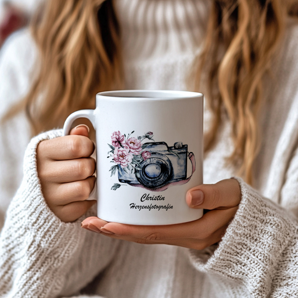 Personalisierte Fotografin-Tasse mit Aquarellkamera und rosa Blumenmotiv, ideales Geschenk für Fotografen, aufgenommen in einer gemütlichen Handszene.