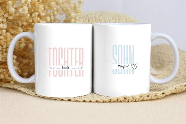 Zwei weiße Tassen mit schlichten Designs. Die linke Tasse trägt den Text „TOCHTER“ in einem zarten Rosaton, mit dem Namen „Gisela“ darunter und dekorativen Linien auf beiden Seiten. Die rechte Tasse zeigt den Text „SOHN“ in einem hellen Blau, mit dem Name