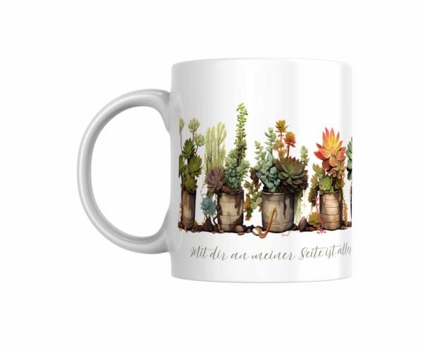 Weiße Tasse mit einer Reihe bunter Sukkulenten in verschiedenen Töpfen und dem Spruch ‚Mit dir an meiner Seite ist alles schöner.‘ Ein liebevolles Geschenk für Pflanzenliebhaber und Menschen, die Naturmotive schätzen.