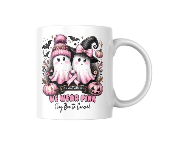 Weiße Tasse mit zwei Geistern, von denen einer eine rosa Mütze und der andere einen Hexenhut trägt, beide mit rosa Schleife als Symbol für den Kampf gegen Brustkrebs. Umgeben von Kürbissen, Fledermäusen und Blumen, mit dem Text ‚We Wear Pink – Say Boo to