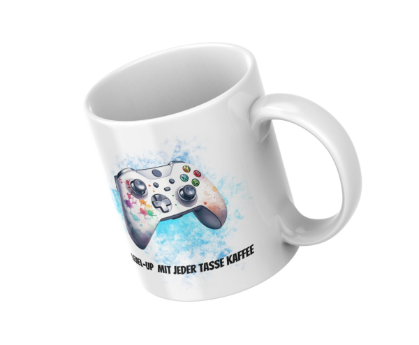 Schräge Ansicht einer weißen Tasse mit einem bunten Gaming-Controller-Design auf blauem Hintergrund. Darunter steht der Text 'Level-Up mit jeder Tasse Kaffee'. Ein perfektes Geschenk für Gamer, die ihre Liebe zum Spielen mit einem täglichen Kaffeeritual v