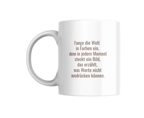 Eine weiße Keramiktasse mit einem inspirierenden Zitat, das in eleganter, brauner Schrift geschrieben ist. Der Text lautet: "Fange die Welt in Farben ein, denn in jedem Moment steckt ein Bild, das erzählt, was Worte nicht ausdrücken können." Diese Tasse i