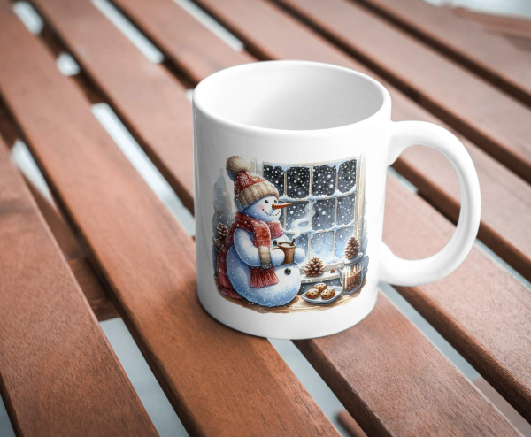 Weihnachtstasse mit Schneemann-Motiv, der am Fenster steht und eine Tasse Kakao hält. Die Tasse ist auf einem Holztisch platziert, mit winterlichen Details wie Tannenzapfen und Keksen im Design. Perfekt für weihnachtliche Gemütlichkeit.