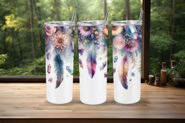 Drei Tumbler mit detailreichen Blumen-, Kristall- und Federdesigns in lebendigen Farben, präsentiert auf einer Holzoberfläche vor einem Fenster mit grünem Waldhintergrund. Perfekt für naturinspirierte Trinkliebhaber.