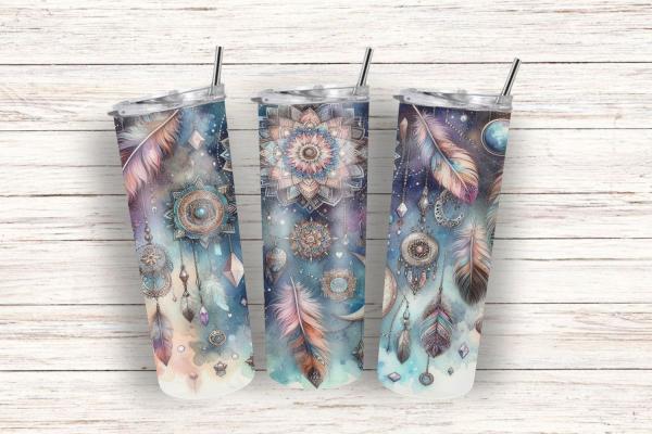 Drei Thermobecher mit einem mystischen Design, das Traumfänger, Federn, Mandalas und geometrische Symbole in sanften Blau- und Beigetönen zeigt. Die Becher stehen auf einem hellen Holzuntergrund und vermitteln eine ruhige, spirituelle Atmosphäre, ideal fü