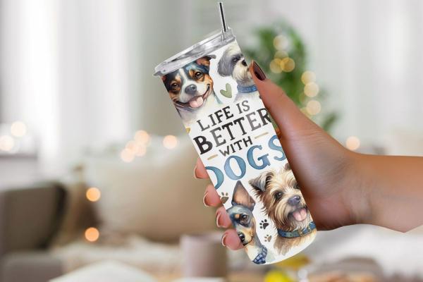 Ein Thermobecher mit dem Design „Life is Better with Dogs“, gehalten von einer Hand vor einem gemütlichen Hintergrund mit unscharfen Lichtern. Der Becher zeigt verschiedene Hunderassen, die fröhlich dreinschauen und mit bunten Schleifen dekoriert sind. Di