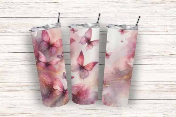 Drei Thermobecher nebeneinander auf einem weißen, strukturierten Holzhintergrund. Die Becher zeigen ein sanftes Design mit rosa Schmetterlingen auf einem weichen, pastellfarbenen Hintergrund, verziert mit subtilen goldenen Akzenten und wolkigen Strukturen