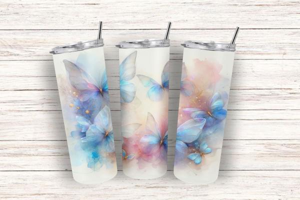 Drei elegante Thermobecher mit einem Design aus pastellfarbenen Schmetterlingen auf einer weißen Holzoberfläche. Die Schmetterlinge in zarten Blau- und Rosatönen verleihen den Bechern eine leichte und verträumte Ausstrahlung.