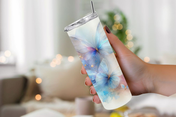 Eine Hand hält einen Thermobecher mit einem verträumten Design aus blauen und rosa Schmetterlingen vor einem verschwommenen, gemütlich eingerichteten Hintergrund mit warmen Lichtern. Die Schmetterlinge scheinen zart und transparent, als würden sie in eine