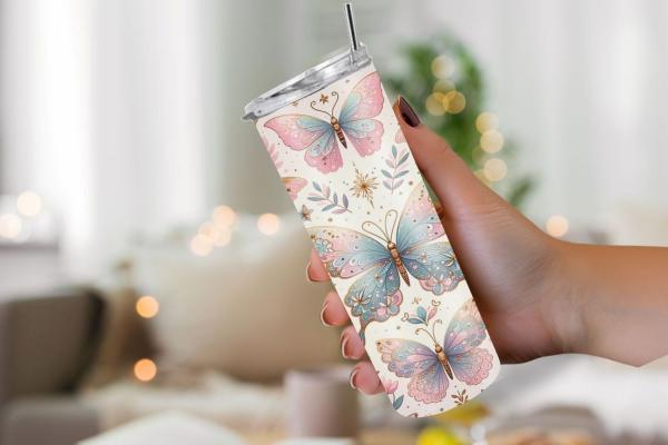 Eine Hand hält einen schlanken Thermobecher mit pastellfarbenem Schmetterlingsdesign. Der Hintergrund zeigt große, detaillierte Schmetterlinge in zarten Rosa- und Blautönen, verziert mit goldenen Akzenten und floralen Elementen, die eine elegante und lebe