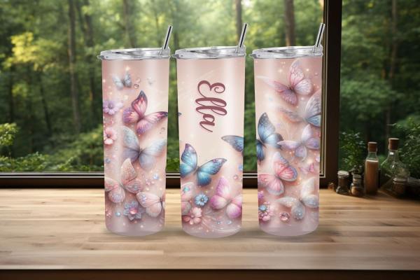 Drei personalisierte Thermobecher mit dem Namen „Ella“, gestaltet in einem romantischen Schmetterlings- und Blumen-Design auf einem pastellfarbenen Hintergrund. Die Becher stehen auf einer Holzoberfläche mit einem Wald im Hintergrund, was das träumerische