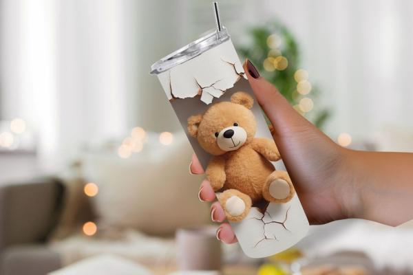 Hand hält einen Thermobecher mit kreativem Design, das einen braunen Teddybär zeigt, der scheinbar durch eine zerbrochene Wand schaut. Der Becher hat einen realistisch dargestellten Riss und der Teddybär sitzt fröhlich in der Mitte des Designs. Im Hinterg