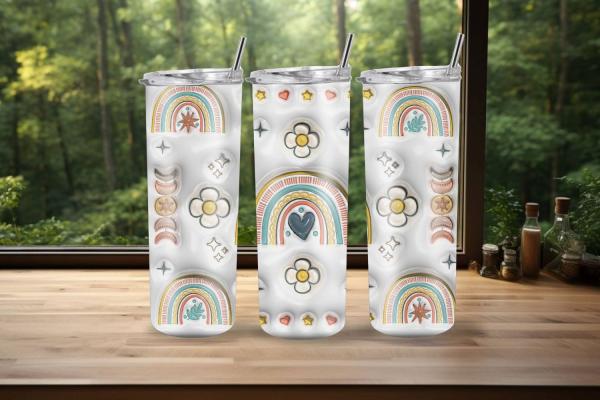 Drei Boho-Tumbler mit bunten Regenbogen-, Blumen- und Herzmotiven, platziert auf einer Holzoberfläche vor einem Fenster mit grünem Waldhintergrund. Perfekt für warme und kalte Getränke im modernen Stil.