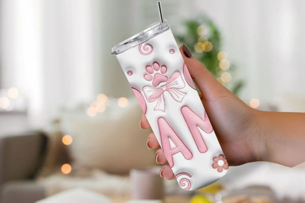 Hand hält einen weißen Thermobecher mit der Aufschrift 'DOG MAMA' in rosa Buchstaben. Der Becher ist mit einem Pfotenabdruck, einer Schleife und Blumenmotiven verziert. Hintergrund zeigt ein gemütliches Wohnzimmer mit unscharfen Lichtern. Perfektes Gesche