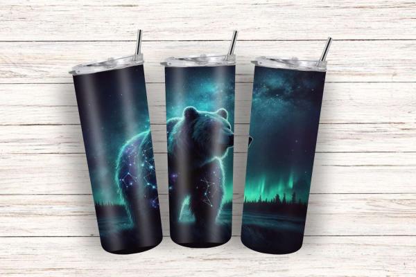 Moderne Reisebecher mit einem Motiv des Nachthimmels und eines Bären, dessen Körper Sterne und Sternbilder zeigt, unter dem Licht des Polarlichts. Der Becher ist mit einem Edelstahlstrohhalm und einem Deckel ausgestattet, und das Design ist in dunklen Bla
