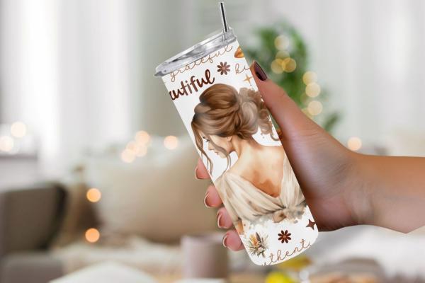 Hand hält einen weißen Thermobecher mit dem Bild einer Frau von hinten und inspirierenden Worten wie 'beautiful' und 'authentic'. Der Becher ist mit Blumen und Naturmotiven verziert. Der Hintergrund zeigt ein gemütliches Wohnzimmer mit weichen Lichtern, i