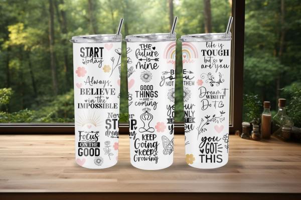 Drei weiße Thermobecher mit motivierenden Zitaten wie 'Believe in the impossible', 'Good things are coming', 'Life is tough but so are you' und 'You got this'. Die Becher sind mit floralen Mustern und sanften Pastelltönen dekoriert und stehen vor einem Wa
