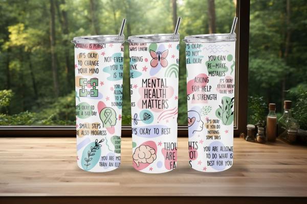 Drei weiße Thermobecher mit Botschaften zur psychischen Gesundheit, wie 'Mental Health Matters', 'It's okay to change your mind', 'Asking for help is a strength' und 'You are allowed to do what is best for you'. Die Becher sind mit beruhigenden Farben und
