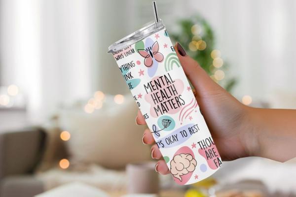 Hand hält einen weißen Thermobecher mit der Aufschrift 'Mental Health Matters' und weiteren positiven Botschaften zur psychischen Gesundheit wie 'It's okay to rest'. Der Becher ist mit Illustrationen von Schmetterlingen, Pflanzen und Gehirnen in beruhigen