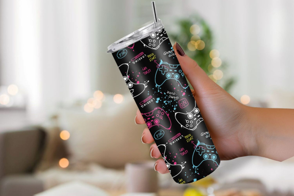 Schlanker Thermobecher in der Hand, mit schwarzem Hintergrund und verspieltem Gaming-Design. Der Becher ist mit weißen Skizzen von Spielcontrollern und farbigen Wörtern wie ‚Press Start‘, ‚Game Over‘ und ‚Never Give Up‘ in Neonfarben wie Blau, Rosa und Ge